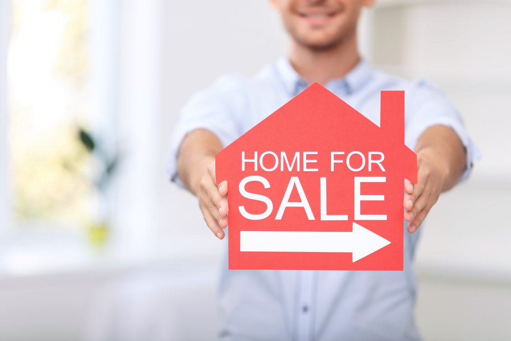 A man holding a Home for Sale sign