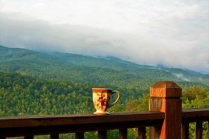 A mug resting on the railing of a deck overlooking the Great Smoky Mountains.